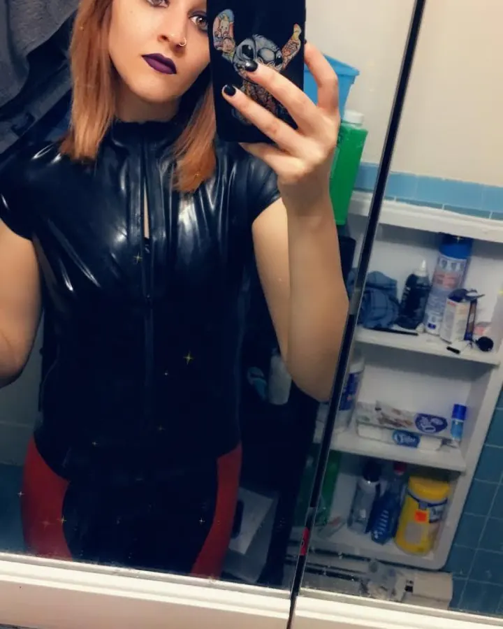 Femme en tenue noire, prenant un selfie dans une salle de bain, regardant l'appareil.