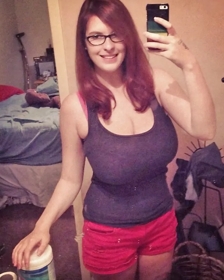 Femme aux cheveux roux prenant un selfie dans un miroir, lunettes, débardeur gris, short rouge