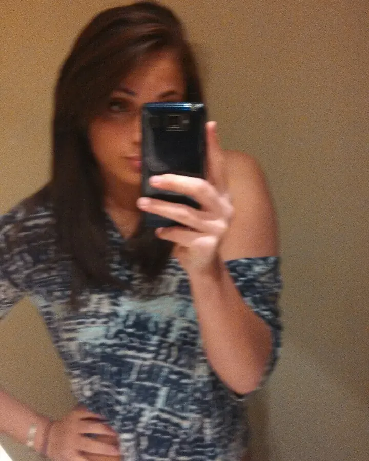 Femme aux cheveux bruns prenant un selfie dans un miroir, portant un haut imprimé bleu et blanc, dans une salle de bain.