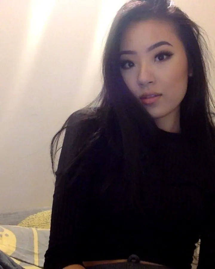 Femme asiatique aux cheveux bruns-noirs, yeux marrons, peau blanche, regard attentif, vêtue d'une tenue simple dans un cadre intime.