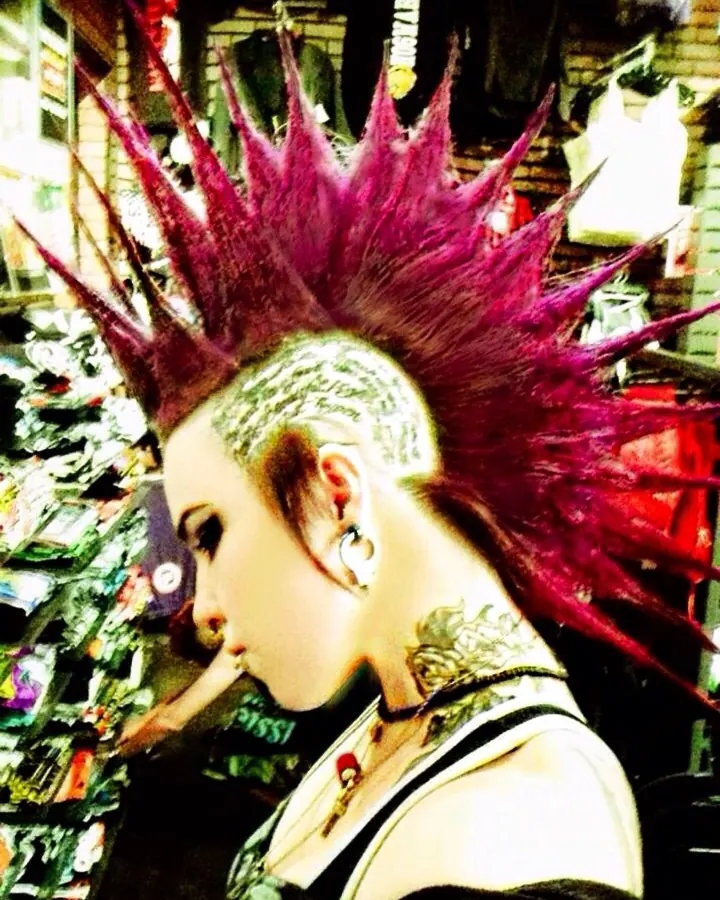 Femme aux cheveux violets, tatouage floral sur le bras, regardant l'objectif, la main sur la joue, sur fond blanc.