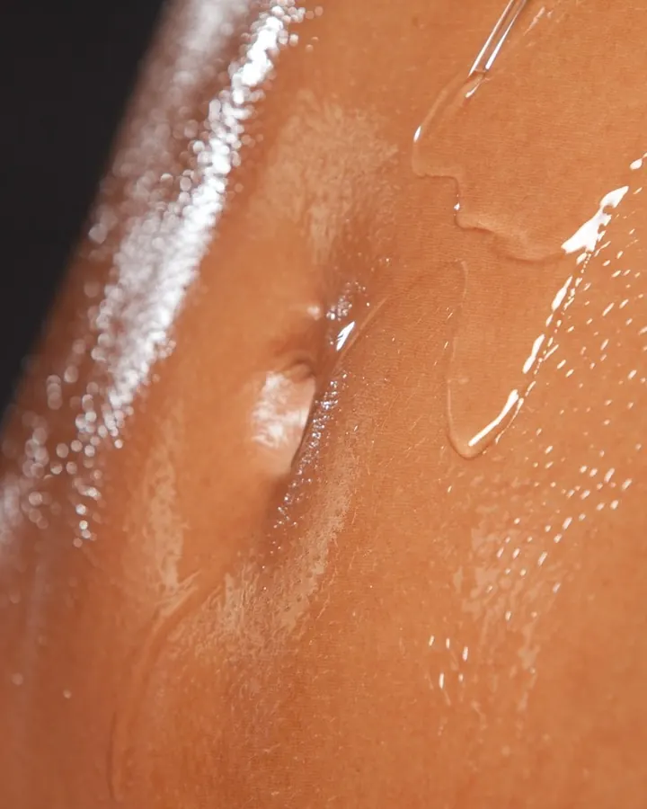Plan rapproché sur un ventre humide, gouttes d'eau coulant, peau bronzée, fond noir.