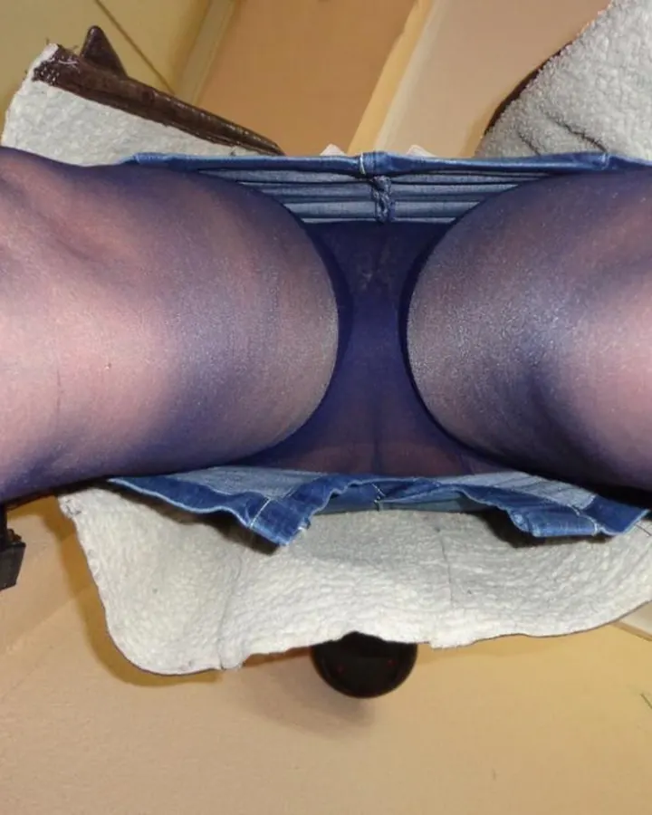 Vue de dessous, jambes en collants foncés sous une jupe en jean, position assise.